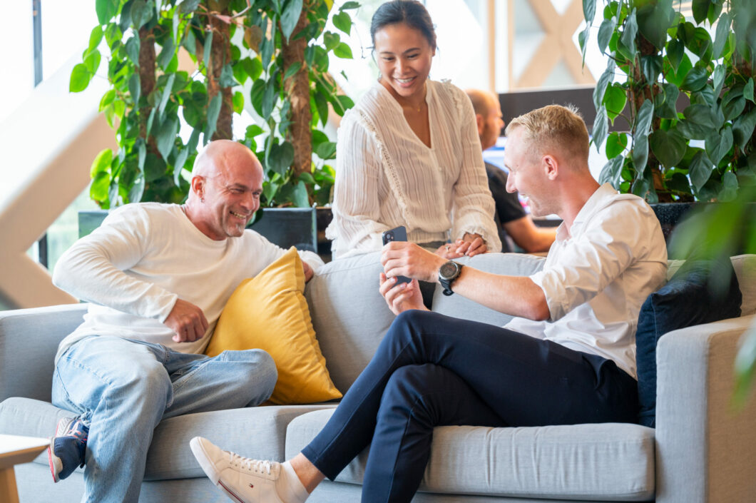 Tre kollegaer ler i sofaen. Foto.